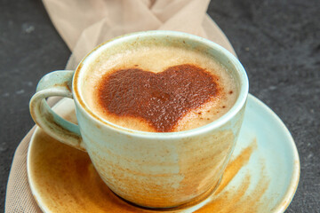 Front close view of a cup of frothy coffee on towel with accessory on dark background