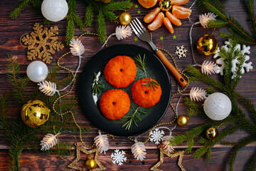 Original serving of snacks. Salad in the form of tangerines in the New Year's decor on a dark wooden table. Top view