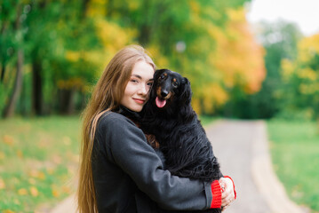 Young attractive woman holding her dachshund dog in her arms outdoors in sunrise in park at autumn