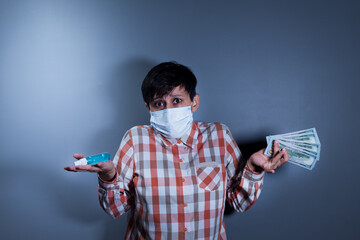 Young woman in medical facial mask is holding sanitizer spray and money on isolated grey background.