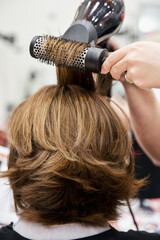 Hairdresser cuts and combs hair with blow dryer to blonde lady