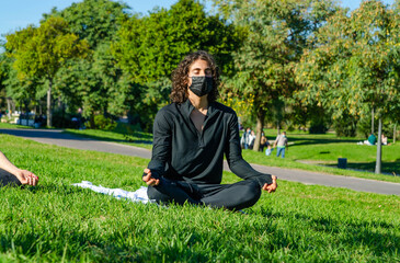 Fototapeta premium Young Attractive Man with Mask Meditating in a Yoga Class at the Park in Summer