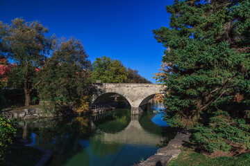 Fototapeta na wymiar Huron Street Bridge, Shakespeare theme garden, Stratford, On, Canada. This stone bridge was built in 1885, is the only double-arched bridge in North America still in use for automotive traffic.