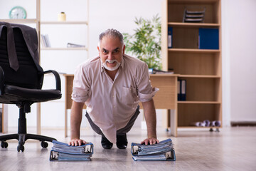 Fototapeta na wymiar Old male employee doing physical exercises at workplace