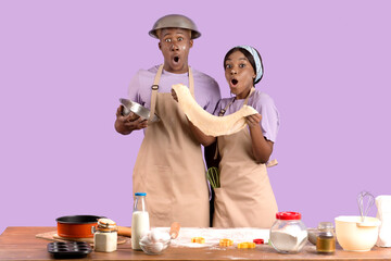 Shocked young black woman with her boyfriend cooking together, having trouble baking on violet studio background