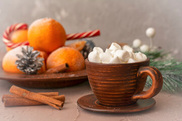 Fototapeta premium Hot coffee with marshmallows in clay cup on table. Tangerines, cinnamon and candy in winter composition. Selective focus, blurred background