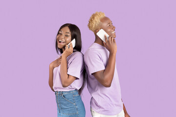 Positive black man and his girlfriend calling on smartphones, having pleasant conversation over lilac studio background