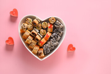 Sushi set in plate as heart on pink background decorated romantic candles. Valentine's day. Space for text. Food delivery.