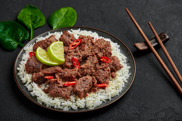 Beef Rendang on black plate at black slate table top. Indonesian padang cuisine meat dish. Asian food.