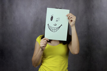 girl covers her face with a smiley face on a piece of paper