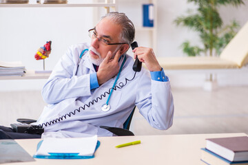 Old male doctor talking by telephone in the clinic