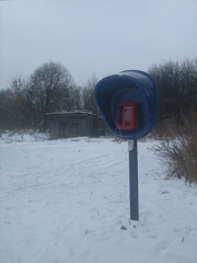 A new phone booth with a payphone in an abandoned village on the background of an abandoned building. In the Russian province on a cloudy winter day.