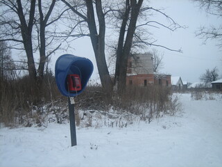 A new phone booth with a payphone in an abandoned village on the background of an abandoned building. In the Russian province on a cloudy winter day.