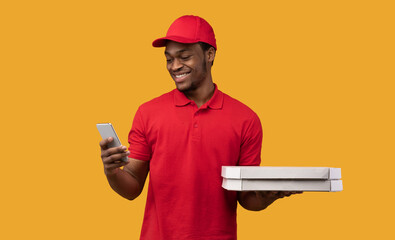 Black delivery man holding pizza boxes, using smartphone