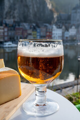 Drinking of dark and strong Belgian abbey beer with cheeses with nice view on Maas river and town Dinant, Belgium