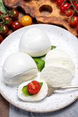 Cheese collection, eating. of white soft Italian cheese mozzarella, served with red cherry tomatoes, fresh basil leaves