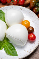 Cheese collection, white balls of soft Italian cheese mozzarella, served with red cherry tomatoes, fresh basil leaves