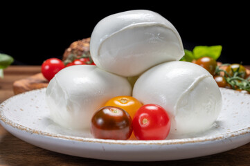 Cheese collection, white balls of soft Italian cheese mozzarella, served with red cherry tomatoes, fresh basil leaves