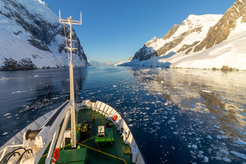 A passenger ship passes the Lemaire Channel at sunset. View of the ship's bow. Antarctica.