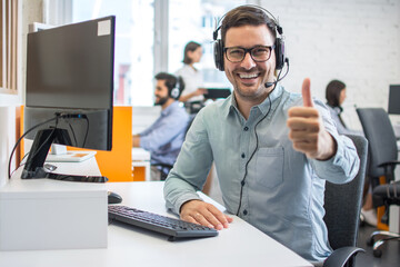 Cheerful handsome call center worker showing thumbs up in a call center.