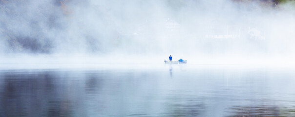 the lonely fisher in the mist, early morning a fisher man wit his boat  surrounded by fog, and the reflection in the water where you can only see the silhouette 