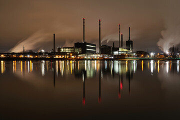 Hell erleuchtetes Industriegeb&auml;ude  in Linz neben der Donau in der Nacht mit hohen qualmenden Schornsteinen