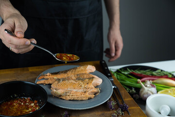 Chief cook is seasoning with chili sauce carved fish baked in salt crust. Seafood cooking. Salmon or seabass under salt crust with vegetables.