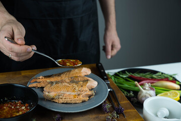Chief cook is seasoning with chili sauce carved fish baked in salt crust. Seafood cooking. Salmon or seabass under salt crust with vegetables.