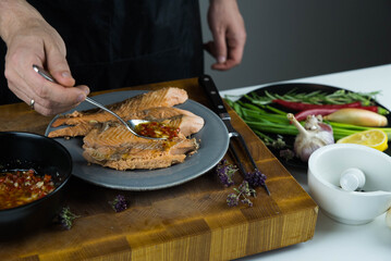 Chief cook is seasoning with chili sauce carved fish baked in salt crust. Seafood cooking. Salmon or seabass under salt crust with vegetables.