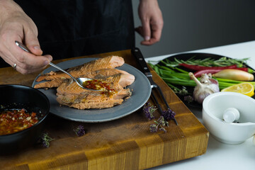 Chief cook is seasoning with chili sauce carved fish baked in salt crust. Seafood cooking. Salmon or seabass under salt crust with vegetables.