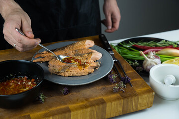 Chief cook is seasoning with chili sauce carved fish baked in salt crust. Seafood cooking. Salmon or seabass under salt crust with vegetables.