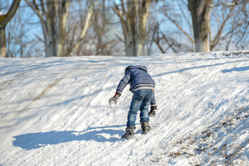 Fototapeta na wymiar The boy is trying to climb a hill that is covered in snow and slide off it.