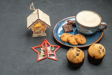 Side view of delicious breakfast with a cup of milk various biscuits cakes and chocolate bars next to new year decorations on dark background