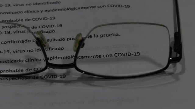 Informe de Covid-19 sobre una mesa y a trav&eacute;s de unas gafas