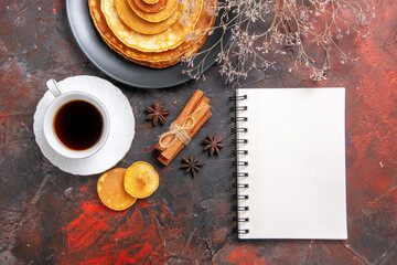 Above view of pluffy pancakes and a cup of tea next to notebook