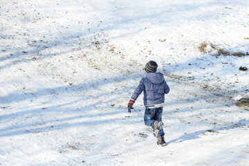 Fototapeta na wymiar The boy runs in winter on a snow-white slide to slide down again.