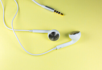 White Earphones lying on the yellow background. Modern music concept. Audio technology. Close up photo.