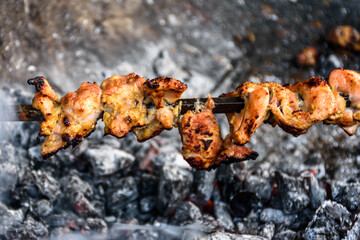 Closeup of skewed chicken legs tandoori slowly cooking over charcoal
