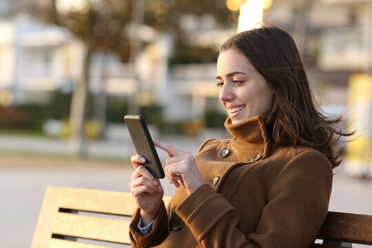 Happy woman in winter using smart phone on a bench