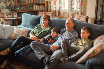 Grandparents and grandchildren sitting on the living room sofa watching television in a rustic and old-fashioned house.