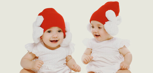 Portrait of two twins baby wearing a winter knitted hat over a white background