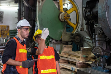 Two factory worker are inspecting sample of metal detail in a factory. Caucasian worker and Asain worker checking sample and Caucasian worker holding tablet and looking at sample in metal factory.