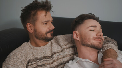 Fototapeta premium Young lovely gay couple cuddling and relaxing on the couch. Different family lifestyle concept Love and care. High quality photo