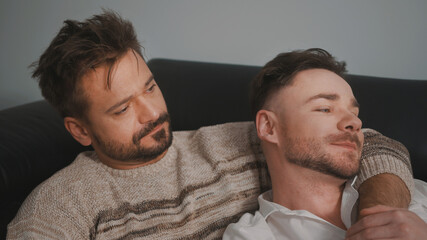 Fototapeta premium Young lovely gay couple cuddling and relaxing on the couch. Different family lifestyle concept Love and care. High quality photo