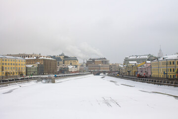 Fototapeta na wymiar view of the Moskva river embankment with historic buildings and frozen water on a cloudy winter day in the old city center and space to copy in Moscow Russia