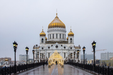 Moscow, Russia, December, 20, 2020: View of the white Cathedral of Christ the Saviour and the bridge with Christmas decorations on a cloudy winter day and space for copying