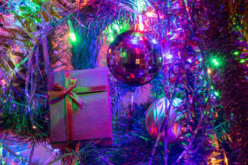 Gift box with a bow on the Christmas tree in colorful lights garlands among Christmas toys.
