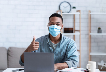 African Man Wearing Mask Sitting At Laptop Gesturing Thumbs-Up Indoor