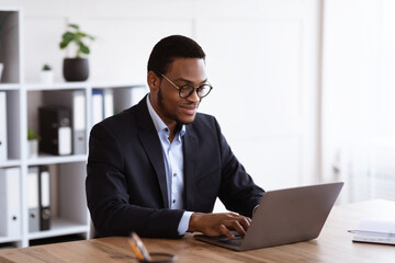 Cheerful black entrepreneur working with laptop, office interior