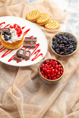 bottom view cake with chocolate on white oval plate bowl with cornels and raisins biscuits on beige tablecloth on marble ground